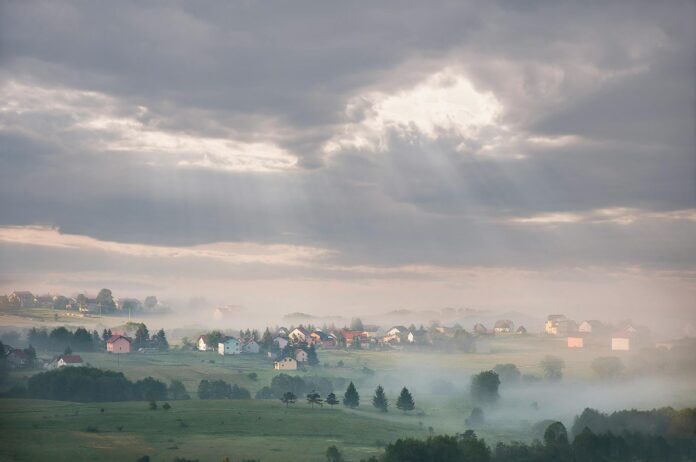 Mglista poranna panorama górskiej wioski z promieniami słońca nad domami Mglista poranna panorama górskiej wioski z promieniami słońca nad domami